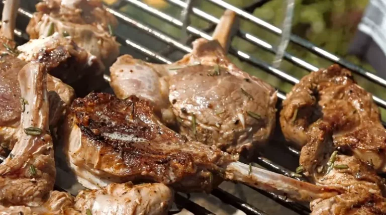 A platter of grilled lamb chops with grill marks, garnished with fresh rosemary and lemon wedges on a rustic table.
