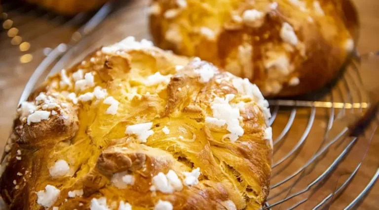 A whole Romanian Pască with a dough cross on top, golden-brown crust, and creamy cheese filling