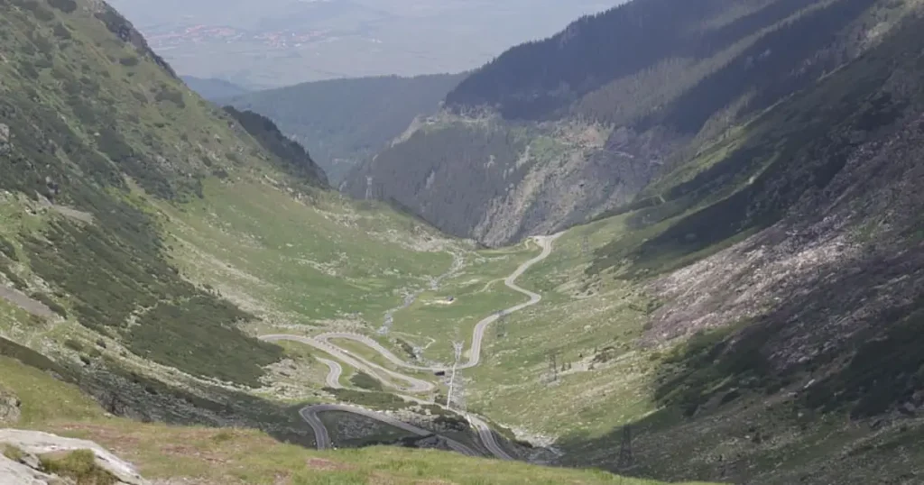 Panoramic view of the Romanian Carpathians featuring the fairy-tale architecture of Peles Castle surrounded by lush green forests.