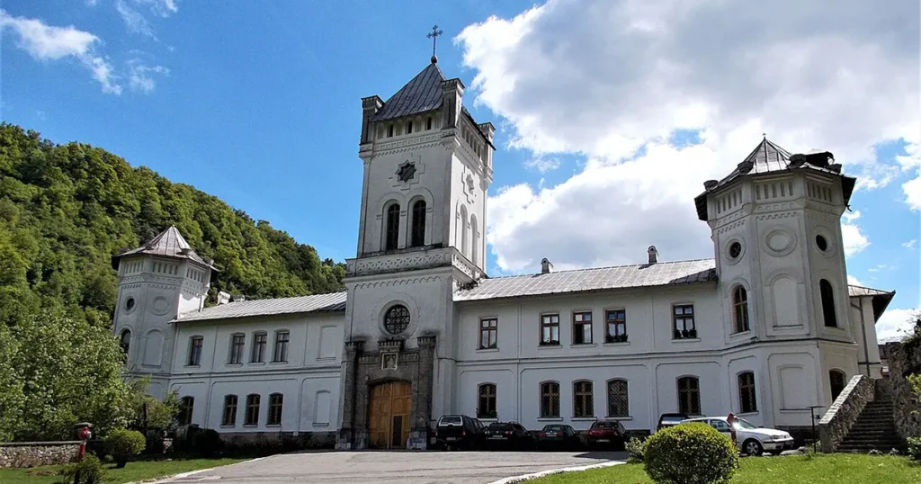The medieval stone architecture of Tismana Monastery set against a backdrop of steep mountains and green forests.