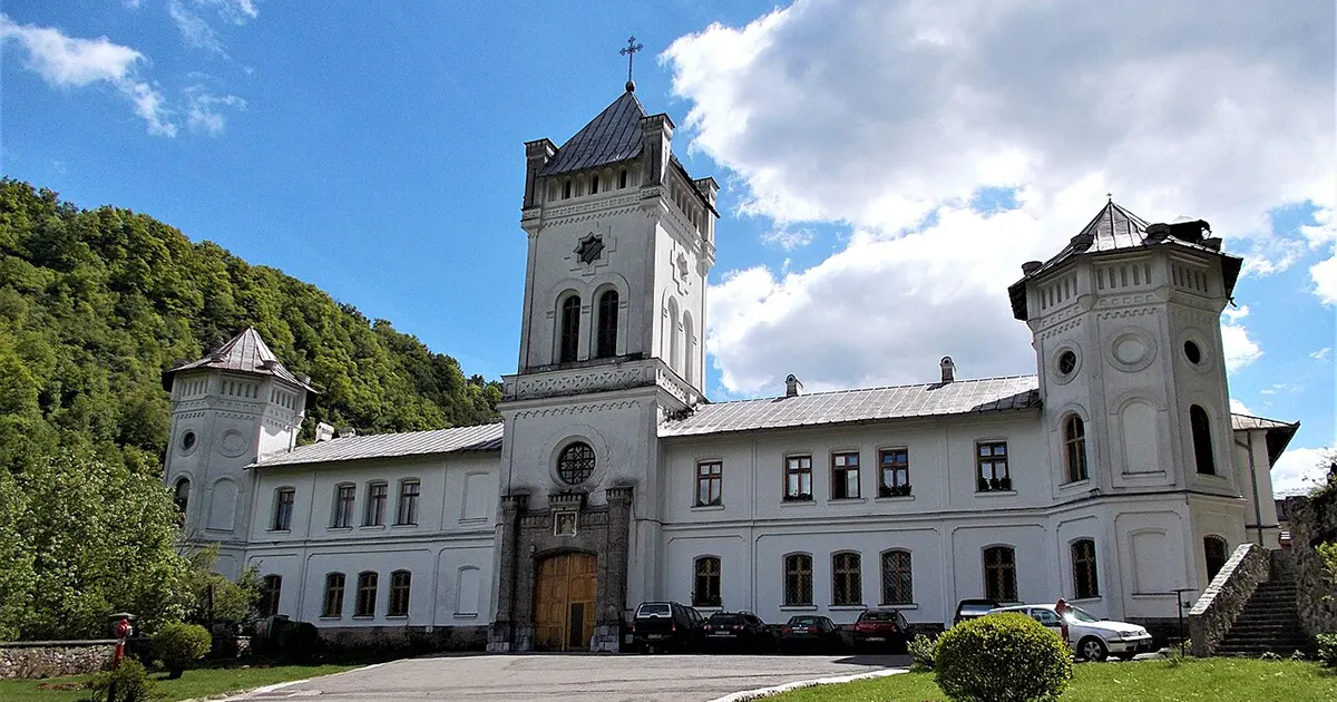 The medieval stone architecture of Tismana Monastery set against a backdrop of steep mountains and green forests.