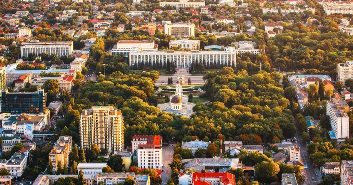 Panoramic view of Chisinau skyline featuring lush green parks, historic architecture, and scenic urban landscape under a blue sky.